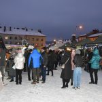 Grupa osób ogląda stoiska na jarmarku na rynku. Panuje zima.