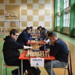 Grupa dorosłych osób na sali gimnastycznej grająca w szachy.