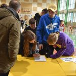 Grupa dorosłych i dzieci w czasie rozgrywek szachowych sprawdzająca wyniki rozgrywek.