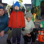 Grupa osób w strojach zimowych, różnej płci i wieku, zebrana na miejskim rynku,.