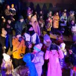 Grupa osób różnej płci i wieku zebrana na rynku. Wszyscy ubrani są w ciepłe, zimowe stroje.