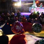 Grupa dzieci na rynku w trakcie zabawy. W tle widać grupe osób w różnym wieku w zimowych strojach oraz scenę. Panuje noc.