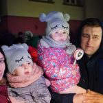 Dorosła kobieta i mężczyzna trzymający na rękach dwie dziewczynki, bliźniaczki. Panuje noc. Wszyscy ubrani są w zimowe stroje.