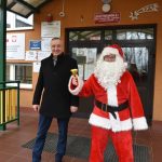 Mężczyzna w stroju mikołaja wraz z drugim mężczyzną w ciemnym stroju stoją przed budynkiem szkoły.