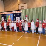 Duża grupa dzieci w mikołajkowych strojach na sali gimnastycznej.