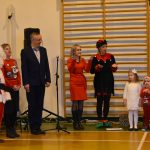 grupa dorosłych w tym mężczyzna w stroju Mikołaja i grupa śpiewających dzieci.