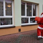 Mężczyzna w stroju Mikołaja macha do dzieci za oknem.