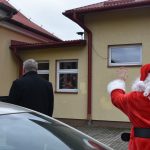 Mężczyzna w stroju Mikołaja macha do dzieci za oknem.