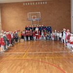 Grupa osób głownie dzieci na sali gimnastycznej. Jeden z dorosłych jest ubrany w strój Mikołaja.