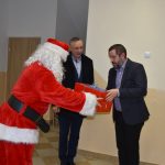 Osoba w stroju Mikołaja wręczająca prezent mężczyźnie w garniturze.