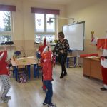 Męzczyzna w stroju mikołaja wita się z dziećmi w sali lekcyjnej.