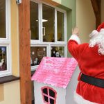 Mężczyzna w stroju Mikołaja macha do dzieci za oknem.