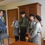 Dorosły mężczyzna w garniturze stoi z grupa dzieci i dorosłą kobietą w strojach harcerskich.