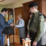 Dorosły mężczyzna otrzymuje upominki od kobiety w harcerskim stroju, Obok stoją harcerze.