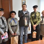 Dorosły mężczyzna w garniturze trzyma duży lampion ze świecą. Towarzyszy mu dorosła kobieta i dwie dziewczynki w harcerskich mundurach.