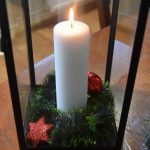 Paląca się świeca umieszczona w dużym, szklanym, prostokątnym lampionie.