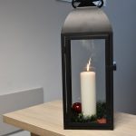 Paląca się świeca umieszczona w dużym, szklanym, prostokątnym lampionie.