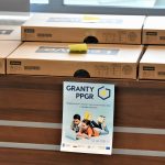 Stół na którym leżą kartonowe paczki. Przyklejony jest do niego plakat.