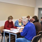 Grupa osób siedząca przy biurku i uzupełniająca dokumenty.