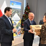 Trzech mężczyzn w garniturach wręczających upominki kobiecie.