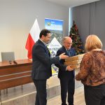 Dwóch mężczyzn w garniturach wręczających upominki kobiecie.