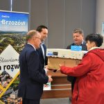 Trzech mężczyzn w garniturach wręczających kobiecie trzy kartonowe pudełka.