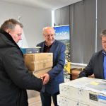 Trzech mężczyzn na sali konferencyjnej trzymający kartonowe pudła.