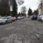 Droga asfaltowa zniszczona, dziurawa i popekana w centrum miasta między budynkami.