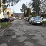 Droga asfaltowa zniszczona, dziurawa i popekana w centrum miasta między budynkami.