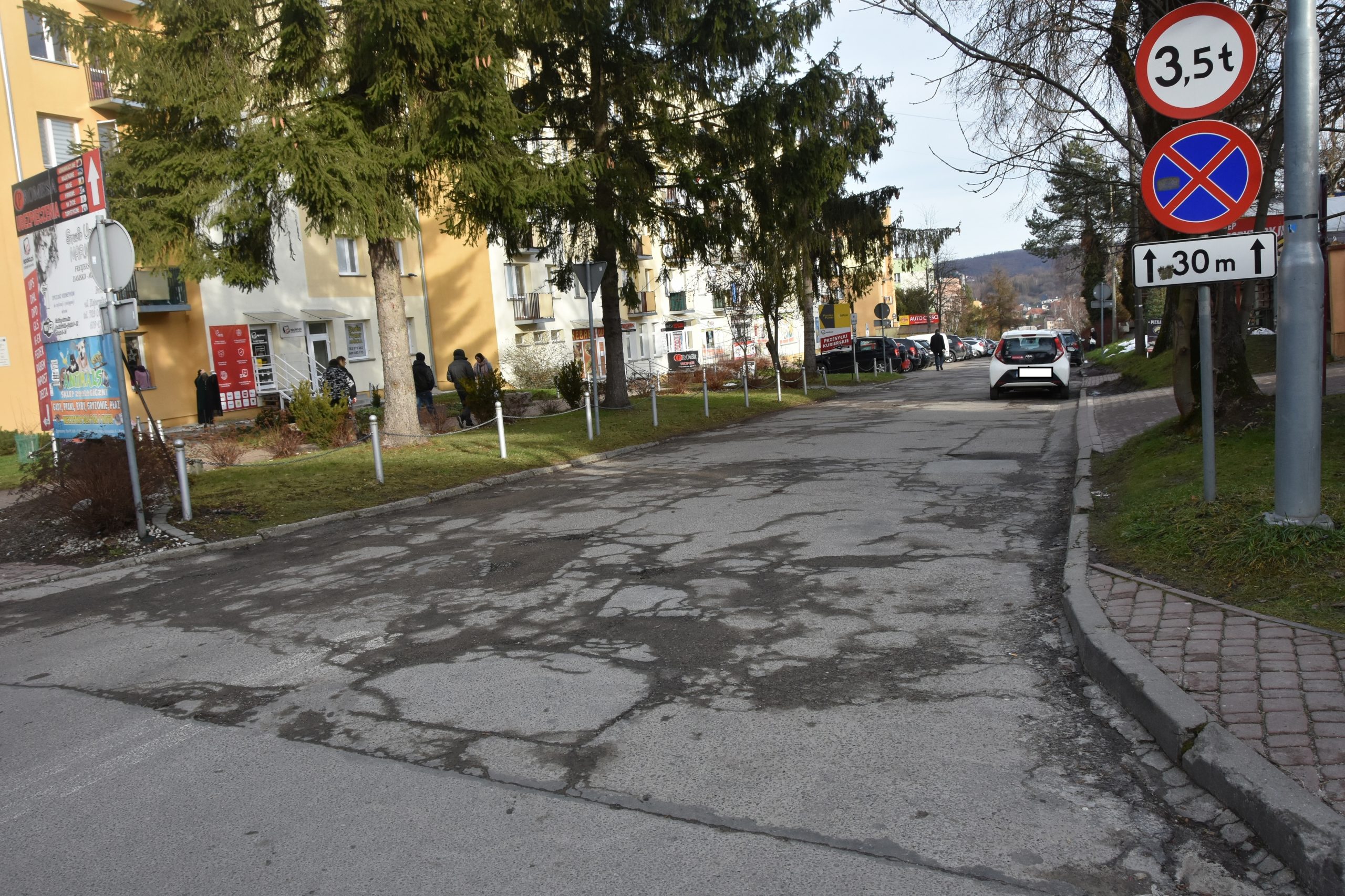 Droga asfaltowa zniszczona, dziurawa i popekana w centrum miasta między budynkami.