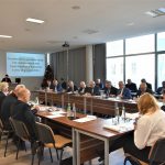 Grupa dorosłych osób róznej płci i wieku zasiadajaca na dużej sali konferenyjnej.