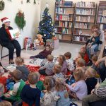 Grupa dzieci słucha kobiety, który siedzi na krzesle i opowiada im bajkę w bibliotece.