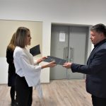 Mężczyzna w garniturze wręcza róże kobiecie na sali konferencyjnej.