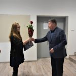 Mężczyzna w garniturze wręcza róże kobiecie na sali konferencyjnej.