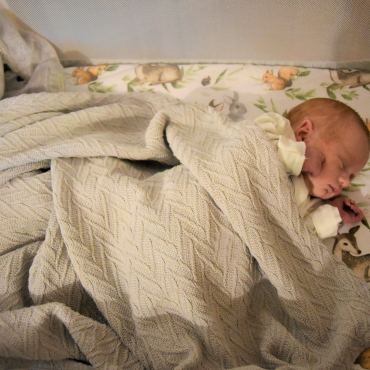 Niemowlę leży w łóżeczku przykryte kocem.
