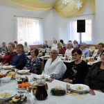 Grupa kobiet ubranych odświętnie siedzi przy nakrytym białym obrusem stole na sali.