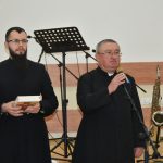 Dwóch mężczyzn w sutannach przemawia do mikrofonu na sali.