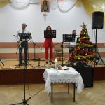 Trzy osoby śpiewają na scenie kolędy.