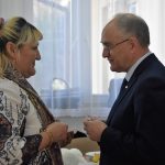 Starszy mężczyzna w garniturze dzieli się opłatkiem ze starsza kobietą.