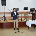 Młopdy mężczyzna w ganiturze przemawia do mikrofonu.