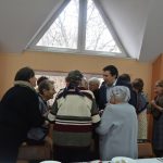 Młody mężczyzna dzieli się opłatkiem ze starszymi kobietami na sali.