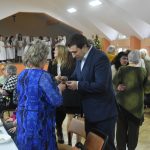 Młody męźczyzna w garniturze dzieli się opłatkiem ze starsza kobietą.