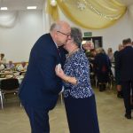 Starszy mężczyzna tuli się ze starsza kobietą w niebieskiej bluzce składając sobie zyczenia.