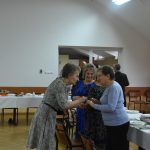 Starsza kobieta dzieli się opłatkiem z dwiema paniami.