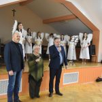 Dwóch męźczyzn i starsza kobieta przemawiają do mikrofonu na sali.