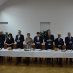 Grupa osób stoi nad stołym nakrytym białym obrusem i się modli.