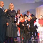 Dorośli męzczyzna i kobieta w oficjalnych strojach oraz gupa dzieci w jasełkowych strojach na scenie.
