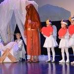 Kobieta i mężczyzna w strojach Józefa I Maryii oraz chłopczyk przebrany za Jezuska i grupa dziewczynek w strojach aniołków na scenie.