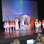 Grupa dorosłych i dzieci w strojach jasełkowych wystepuje na scenie.