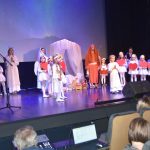 Grupa dorosłych i dzieci w strojach jasełkowych wystepuje na scenie.